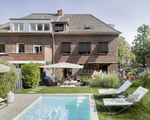 Entspannender Garten mit Pool und stilvollem Backsteinhaus Modernes Backsteinhaus mit Pool und Liegestühlen im Garten